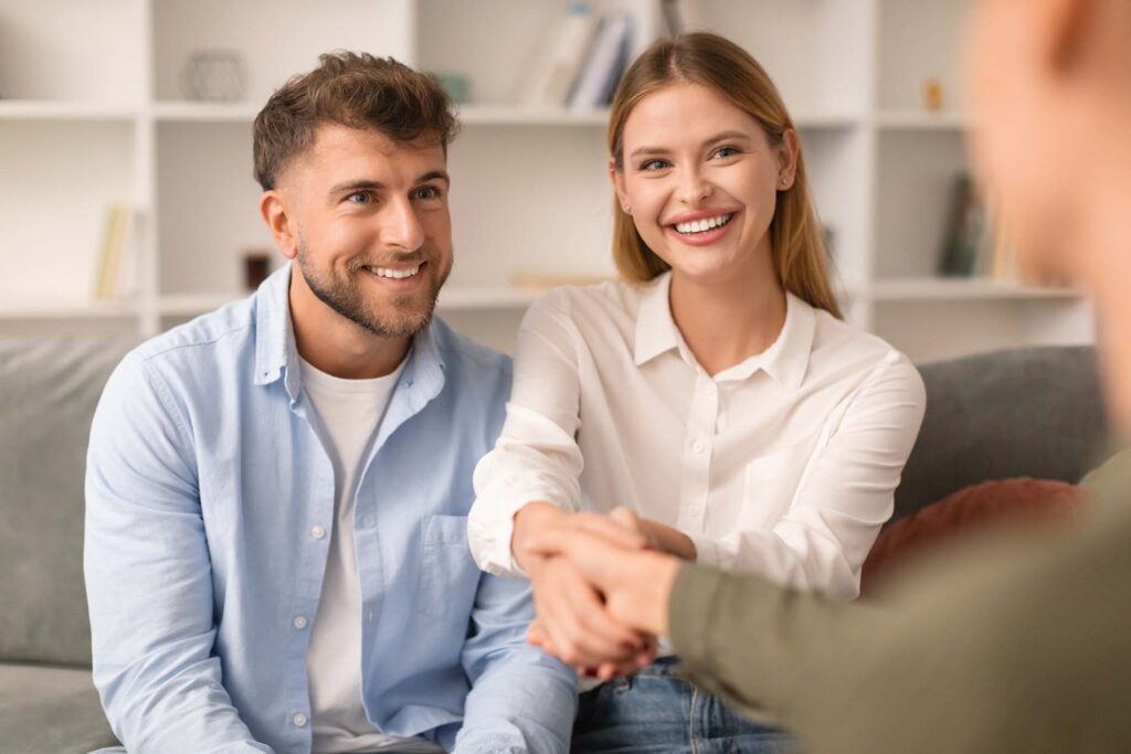 Couples therapy. Grateful husband and wife shaking hands with their therapist at psychologist's office, marking successful resolution to their marital issues during a counseling session