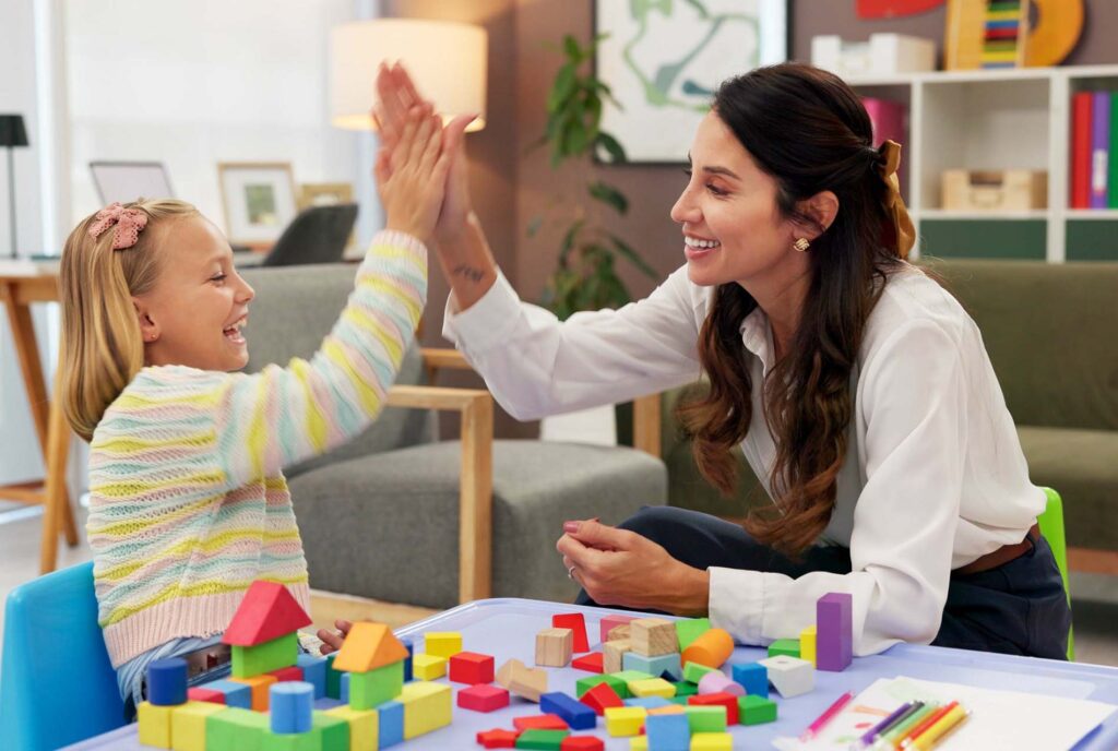 Therapist, child and building blocks for high five, celebration and progress in office. Psychologist woman, pediatrics and girl for toys, clinic or consultation for patient support or development